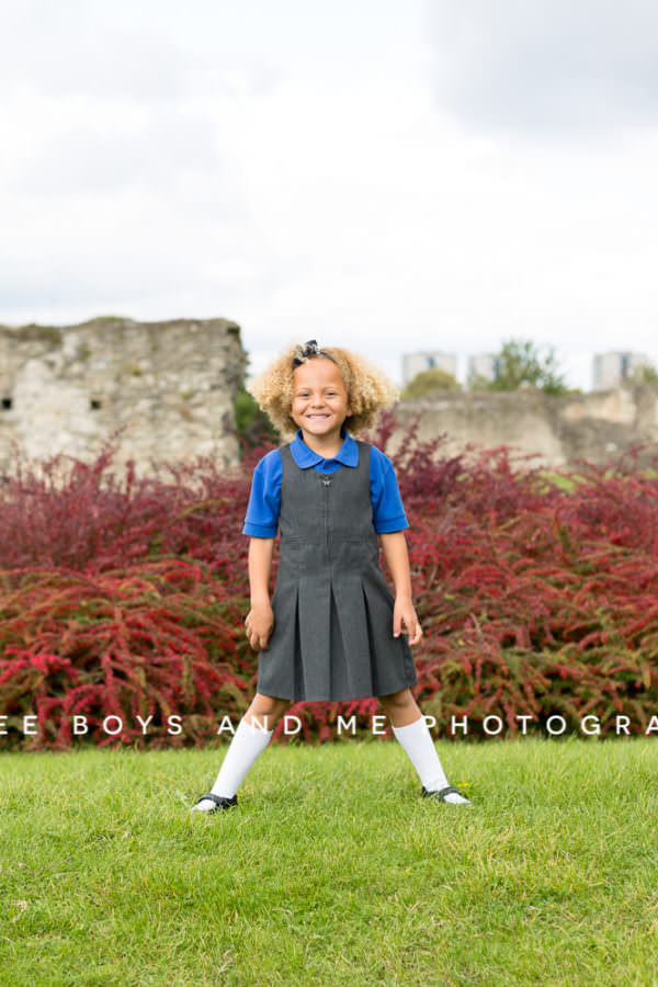 little girl standing in front of red berry hedge at her back to school mini shoot