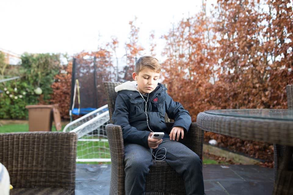 soon to be teenager sitting in the garden listening to music on his phone Sevenoaks Family photographer 3 Boys and Me Photography