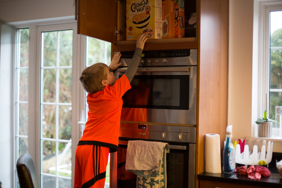 boy reaches to put cornflakes in cupboard Sevenoaks Family photographer 3 Boys and Me Photography