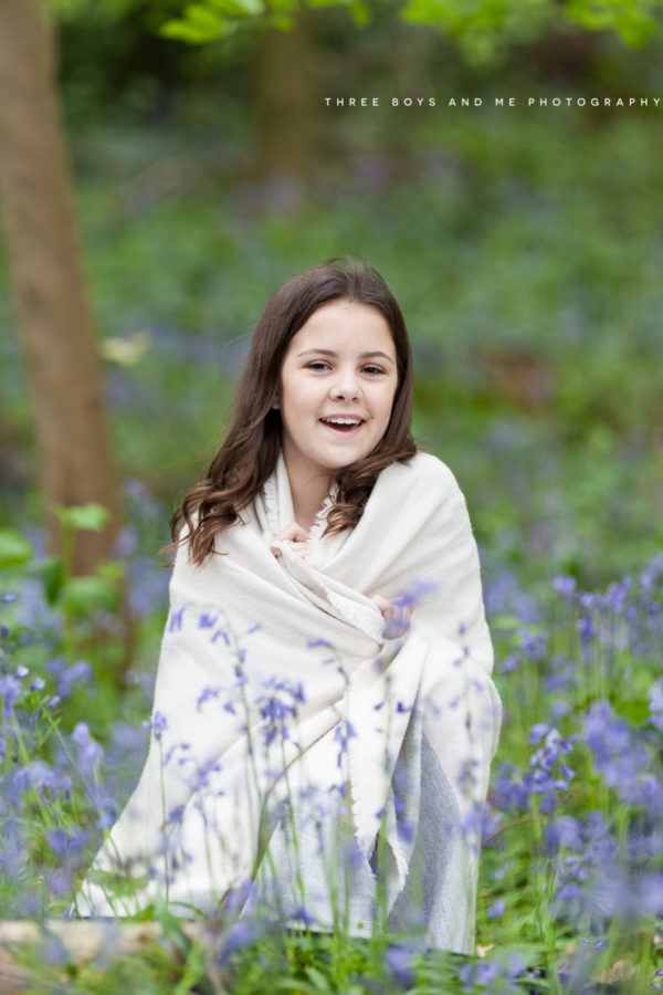 older girl wrapped in scarf smiling sat in the bluebells at her kent bluebell photoshoot in sevenoaks