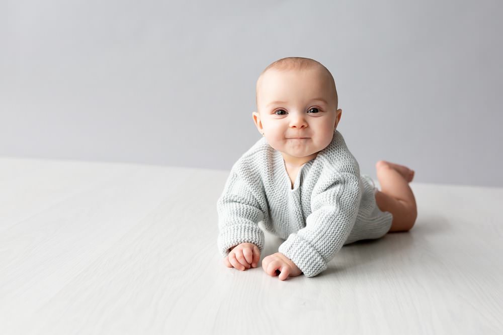 baby girl laying on tummy wearing grey Zara jumper at her baby photograph shoot in Bexley studio