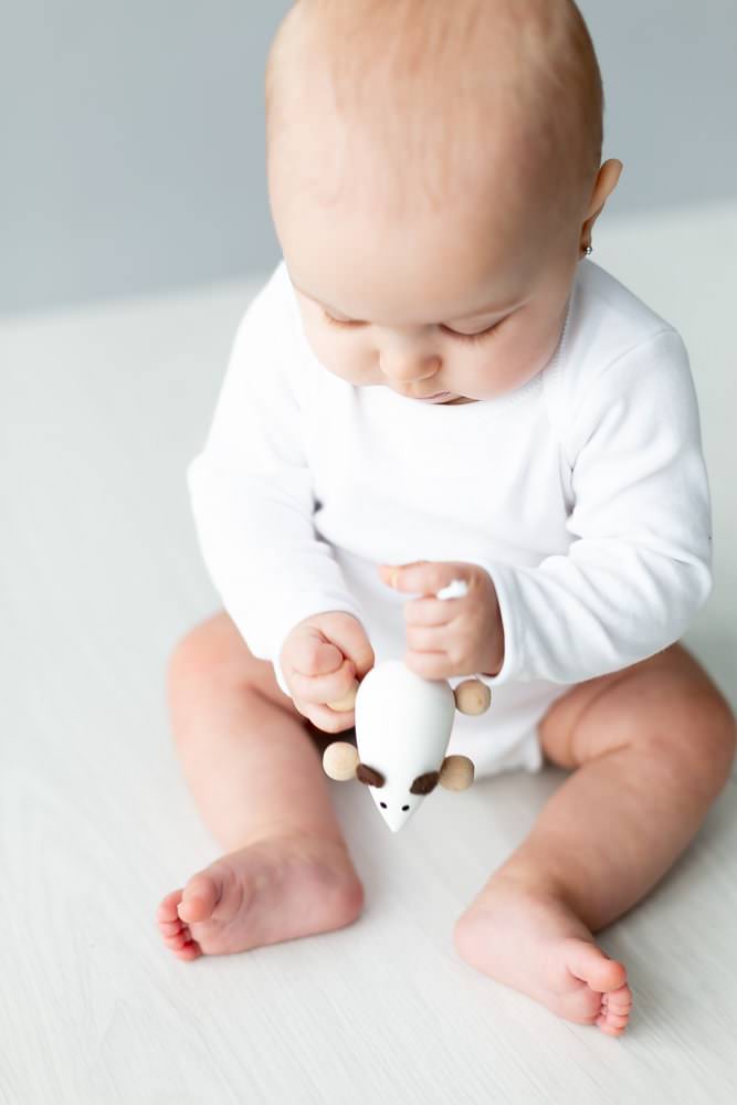 baby girl wearing white with a white wooden mouse at her baby photoshoot in Bexley studio