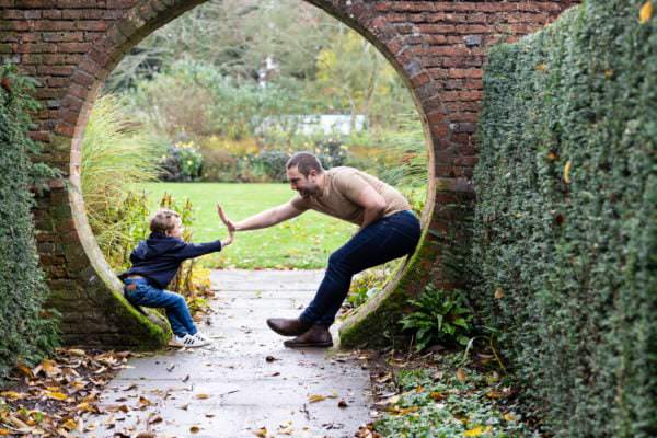 dad and son share a high five in a stone arch at their Sevenoaks family photoshoot