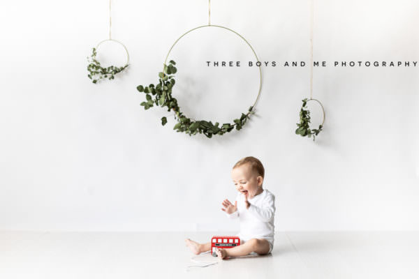 little boy clapping hands, with a red pull along bus at his bexley christmas photoshoot