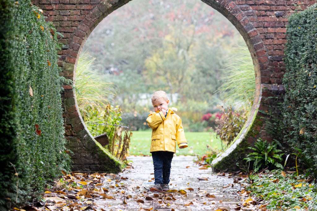 little boy in a yellow coat framed in a brick archway at his sevenoaks autumn photoshoot