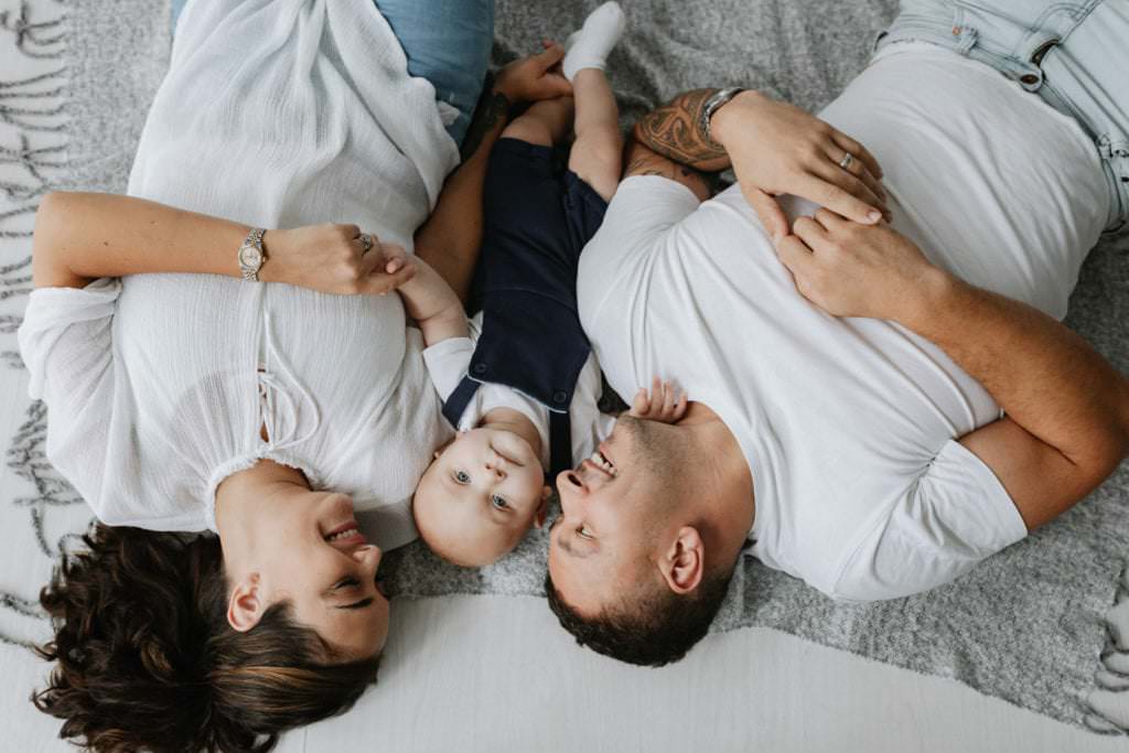 mummy, daddy and baby laying on the floor smiling taken at their Bexley baby photoshoot