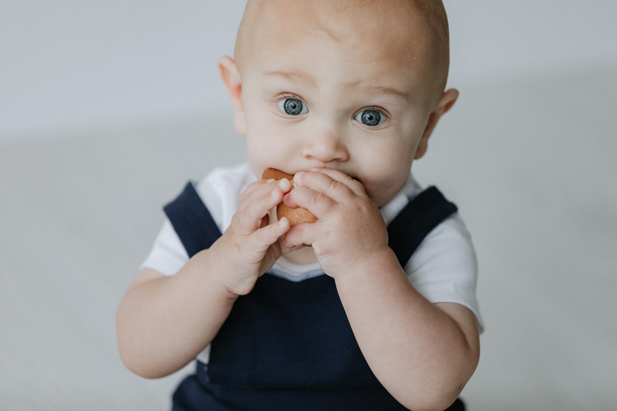 Close up shot of baby with big blue eyes chewing a wooden toy at his Bexley baby photoshoot