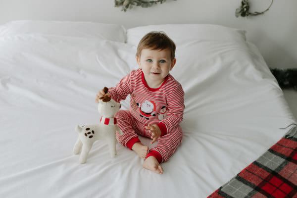 little boy in christmas pjs on a bed at his Bexley Christmas mini photoshoot