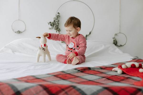 little boy in christmas pjs on a bed at his Bexley Christmas mini photoshoot