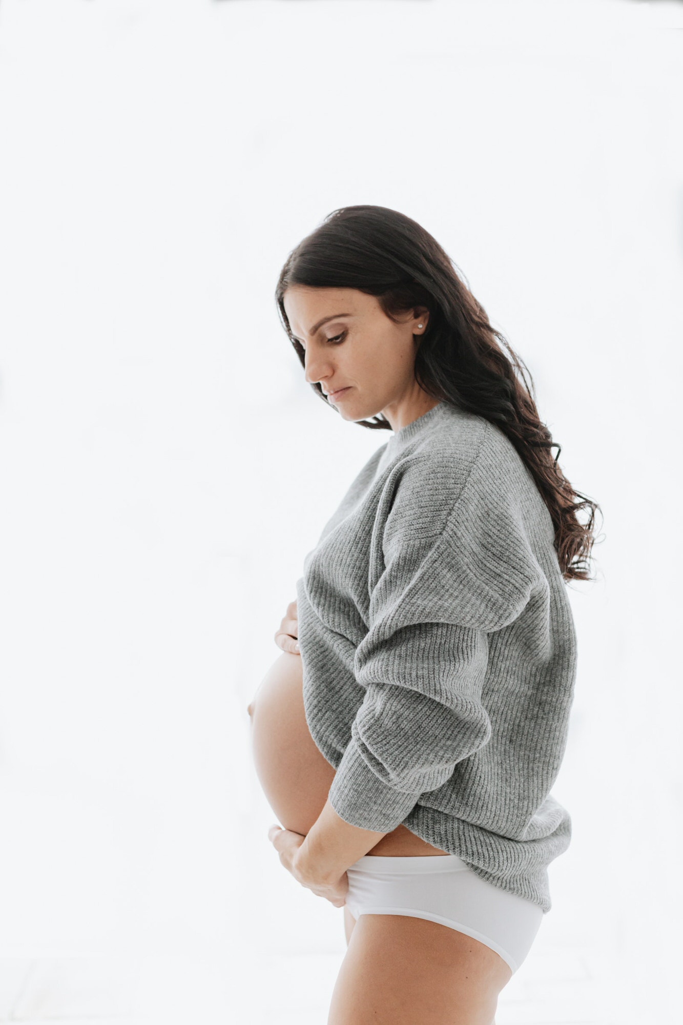 Beautiful mummy to be in grey jumper holding baby bump at her Bexley maternity photoshoot