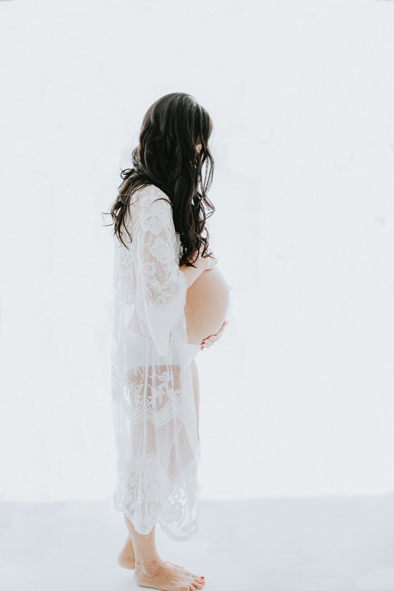beautiful mummy to be in lace dressing gown holding baby bump at her Bexley maternity photoshoot