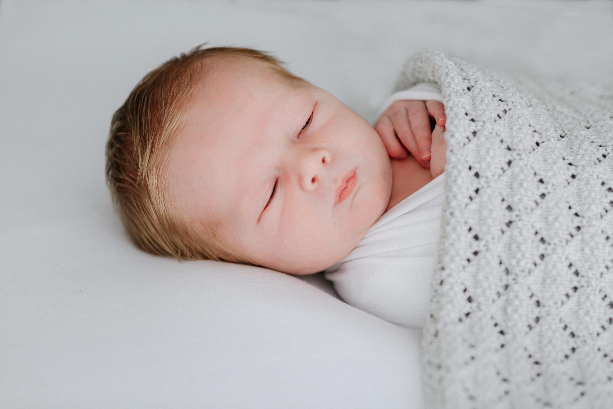 image of newborn baby wrapped in white company blanket at his kent newborn photoshoot in bexley
