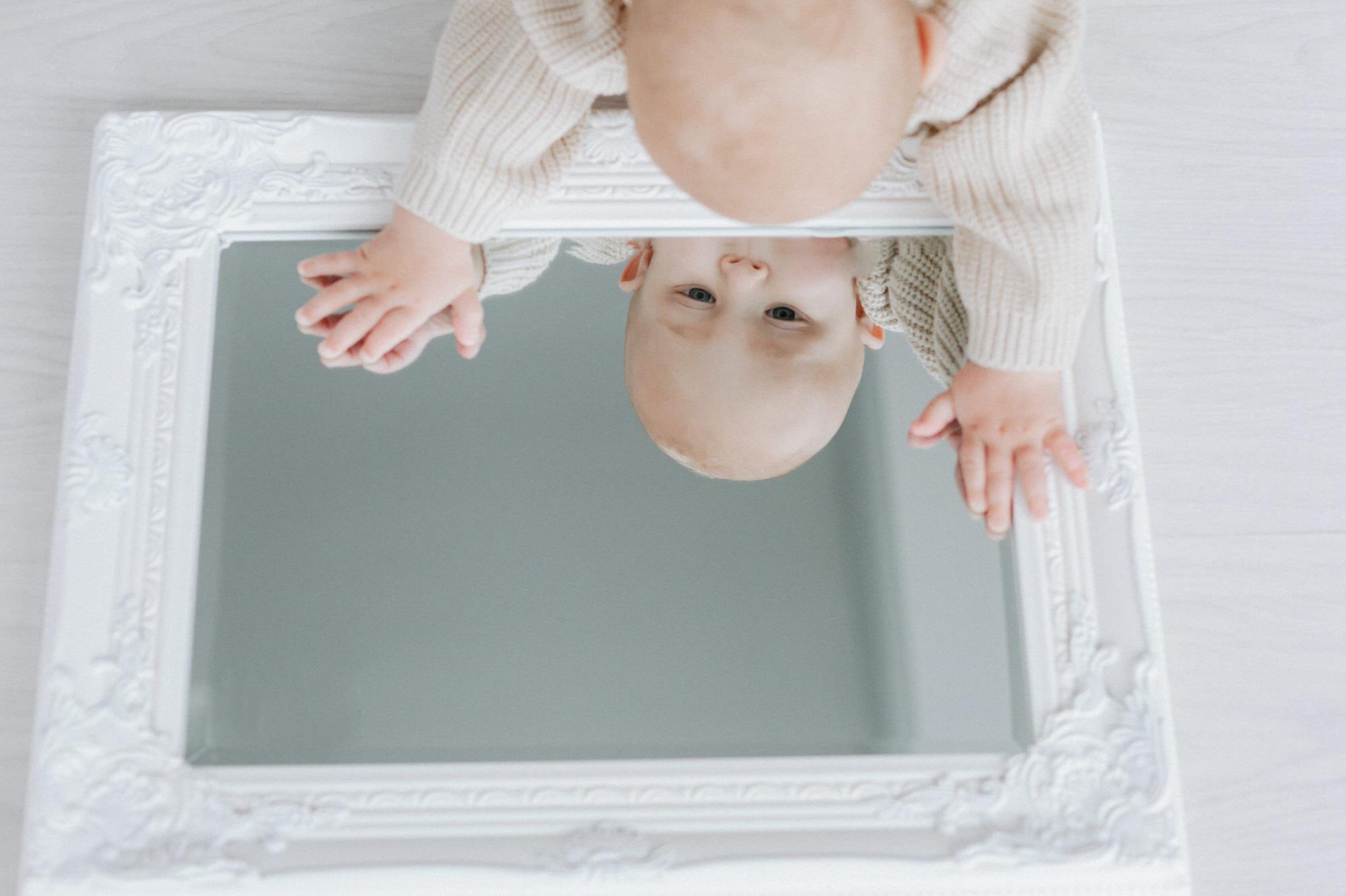 baby boy peering into a mirror on his kent baby photoshoot in bexley