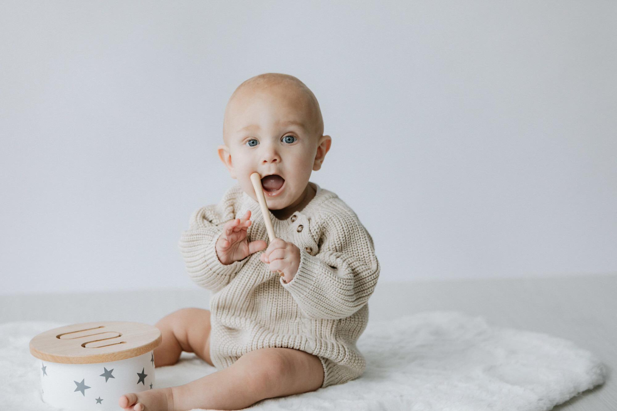 little boy in oversized knitted romper playing with a wooden drum at his Kent sitter photoshoot in Bexley