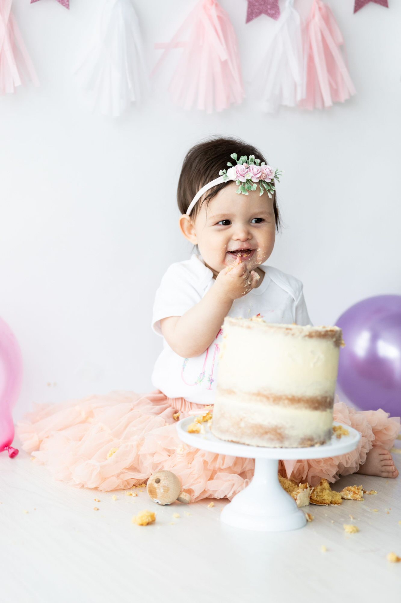 little girl in pink tutu eating cake and smiling at her Kent cake smash photoshoot in Bexley
