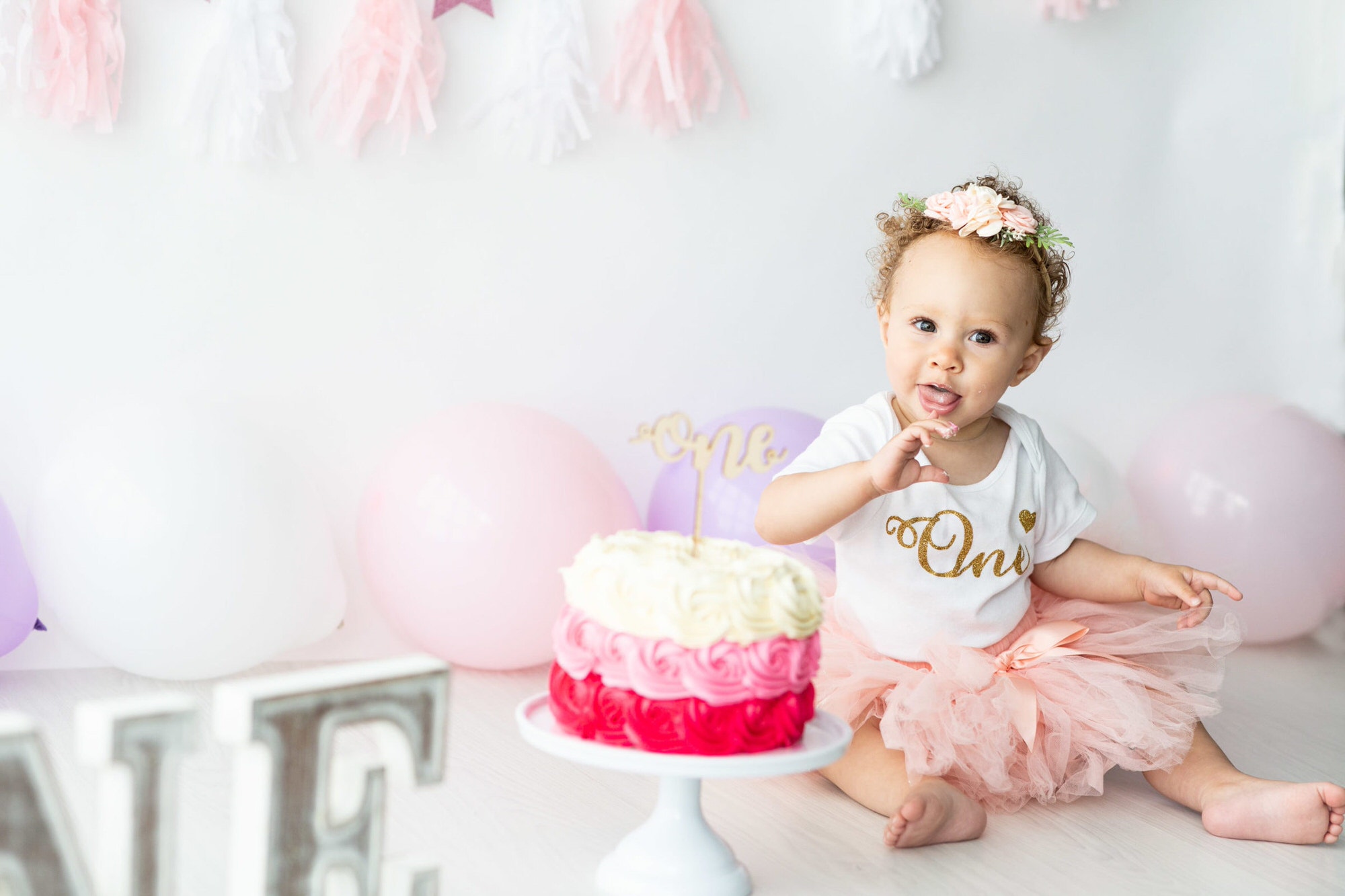 little girl smiles at the camera while eating cake at her Kent cake smash shoot in Bexley