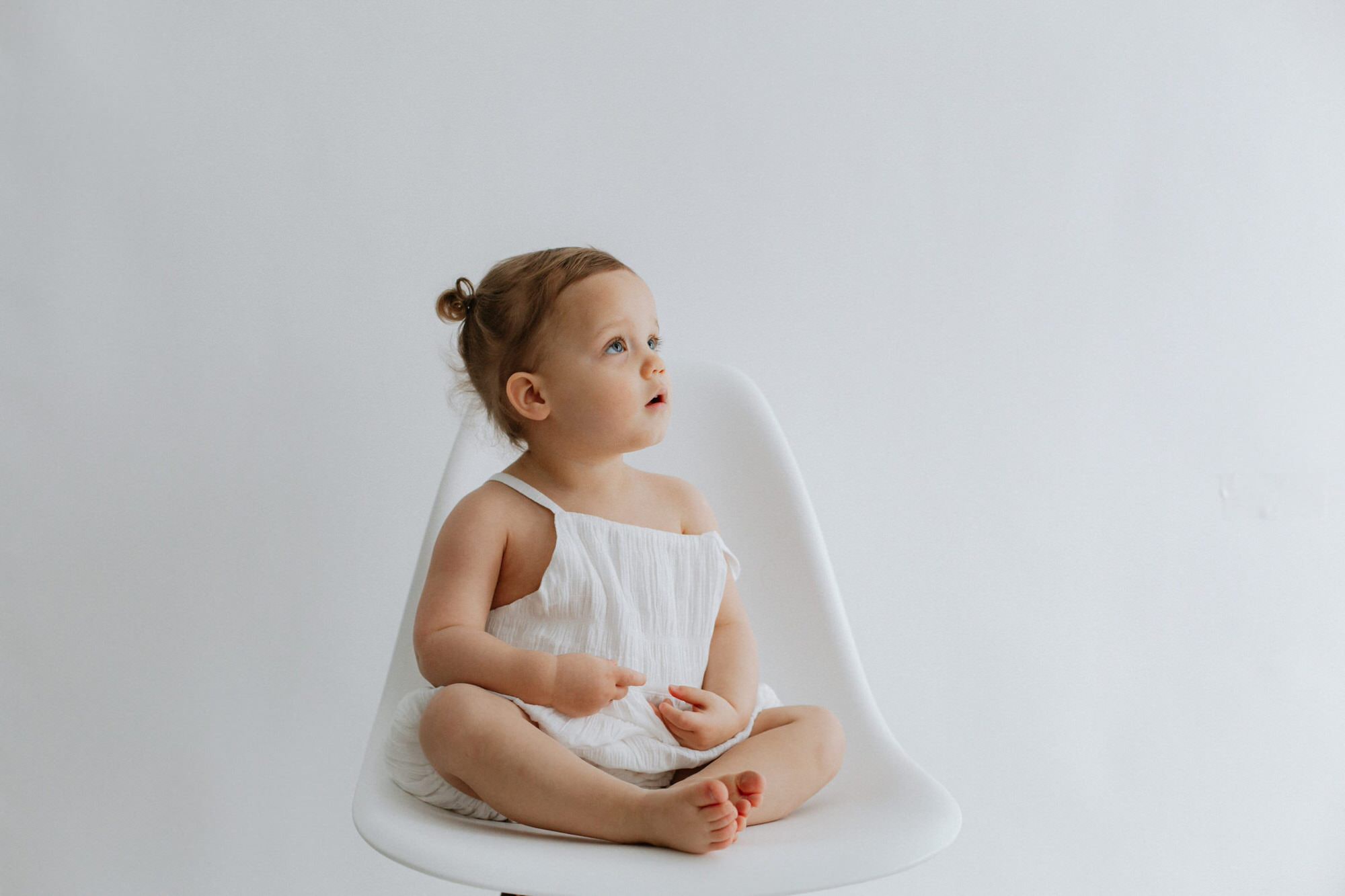 Beautiful image of a baby girl looking up sat in a chair at her Kent baby photoshoot in Bexley