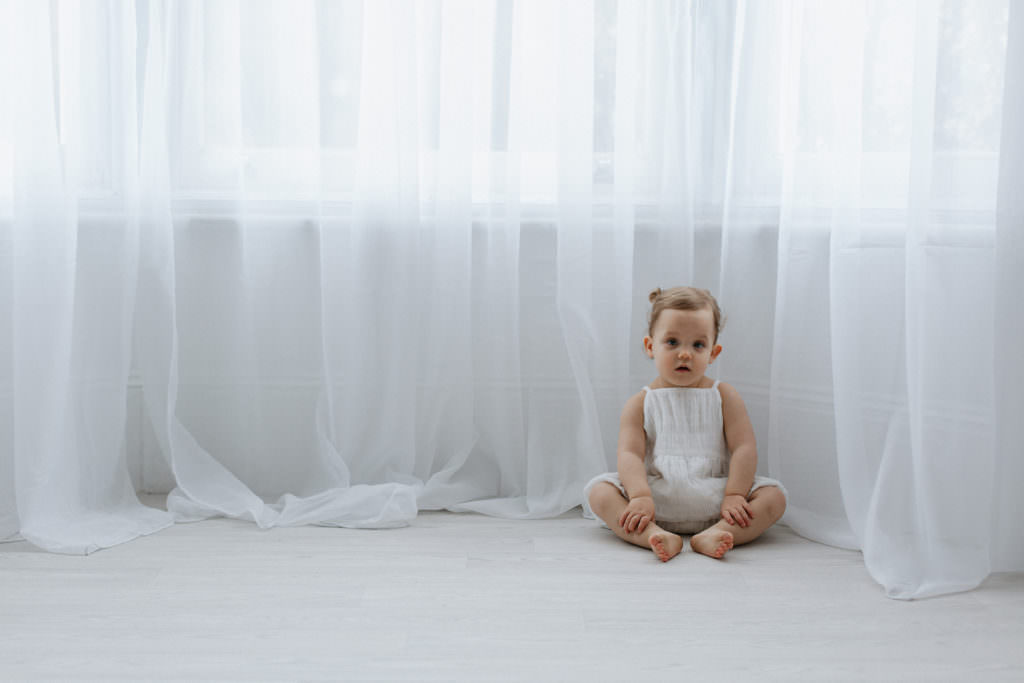 baby girl sat on the floor infant of voile curtains at her Kent baby photoshoot in Bexley