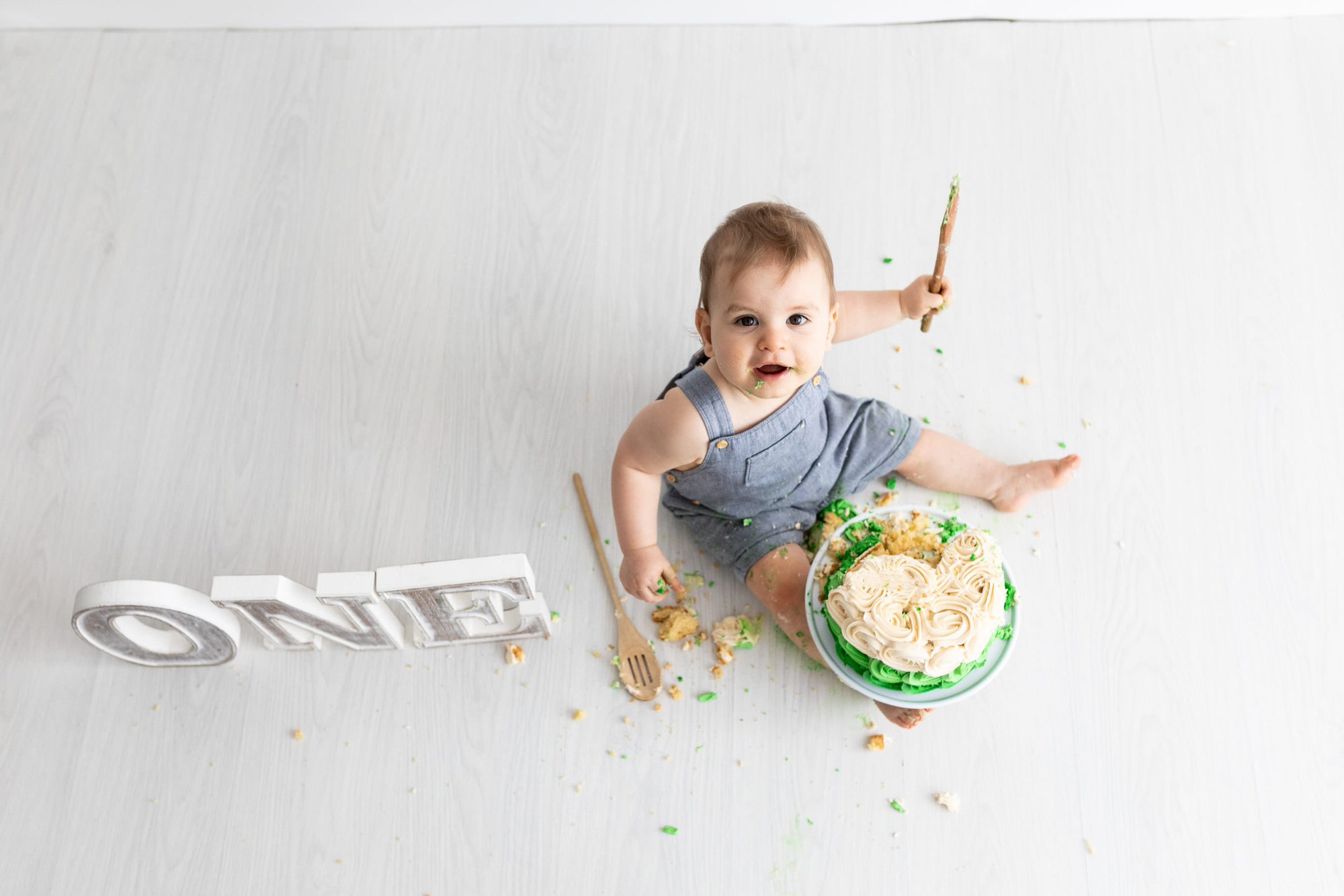 looking down on a little boy with a wooden spoon smashing his cake at his kent cake smash photoshoot in bexley