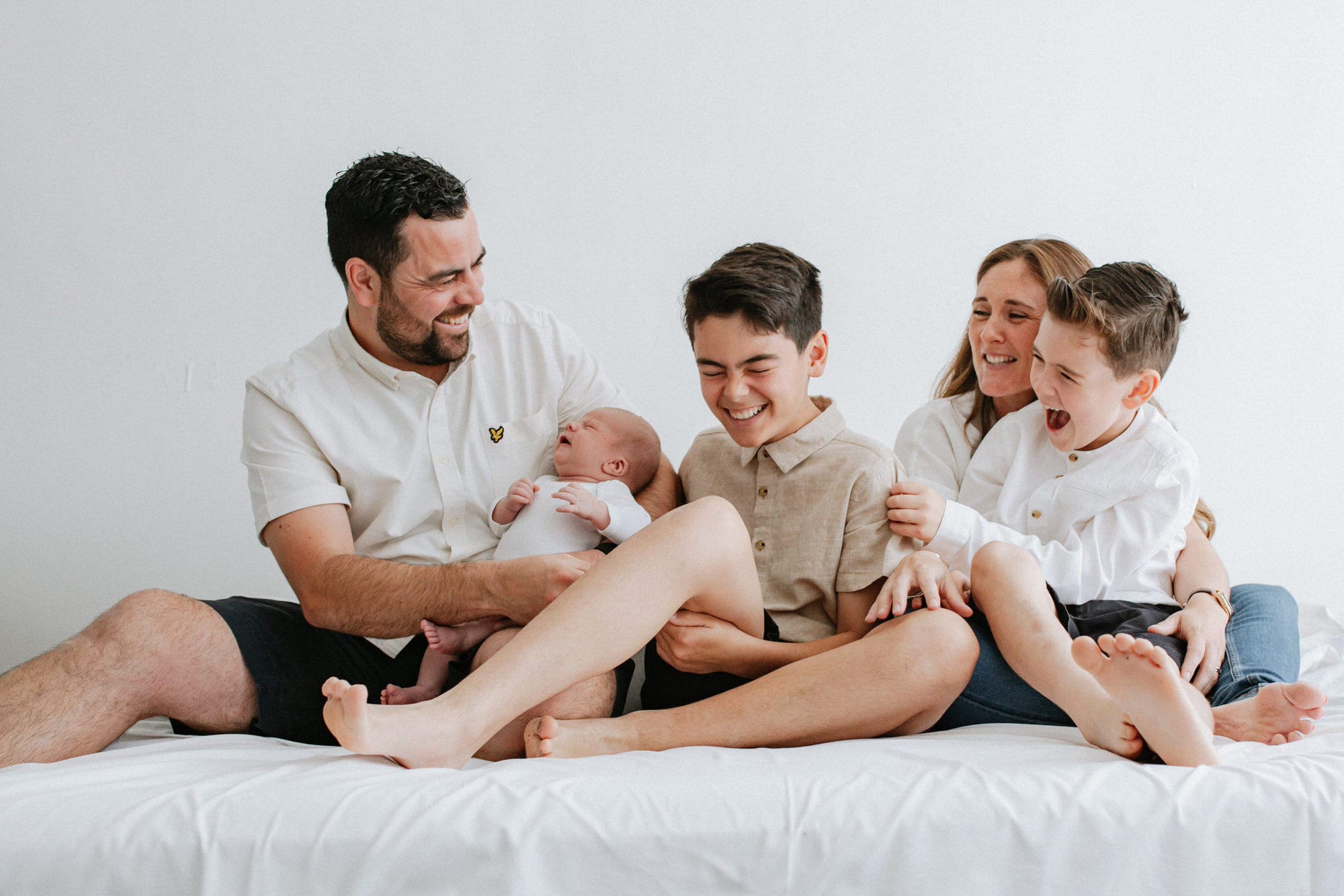 family of five laughing on a bed at their Kent newborn photoshoot in Bexley
