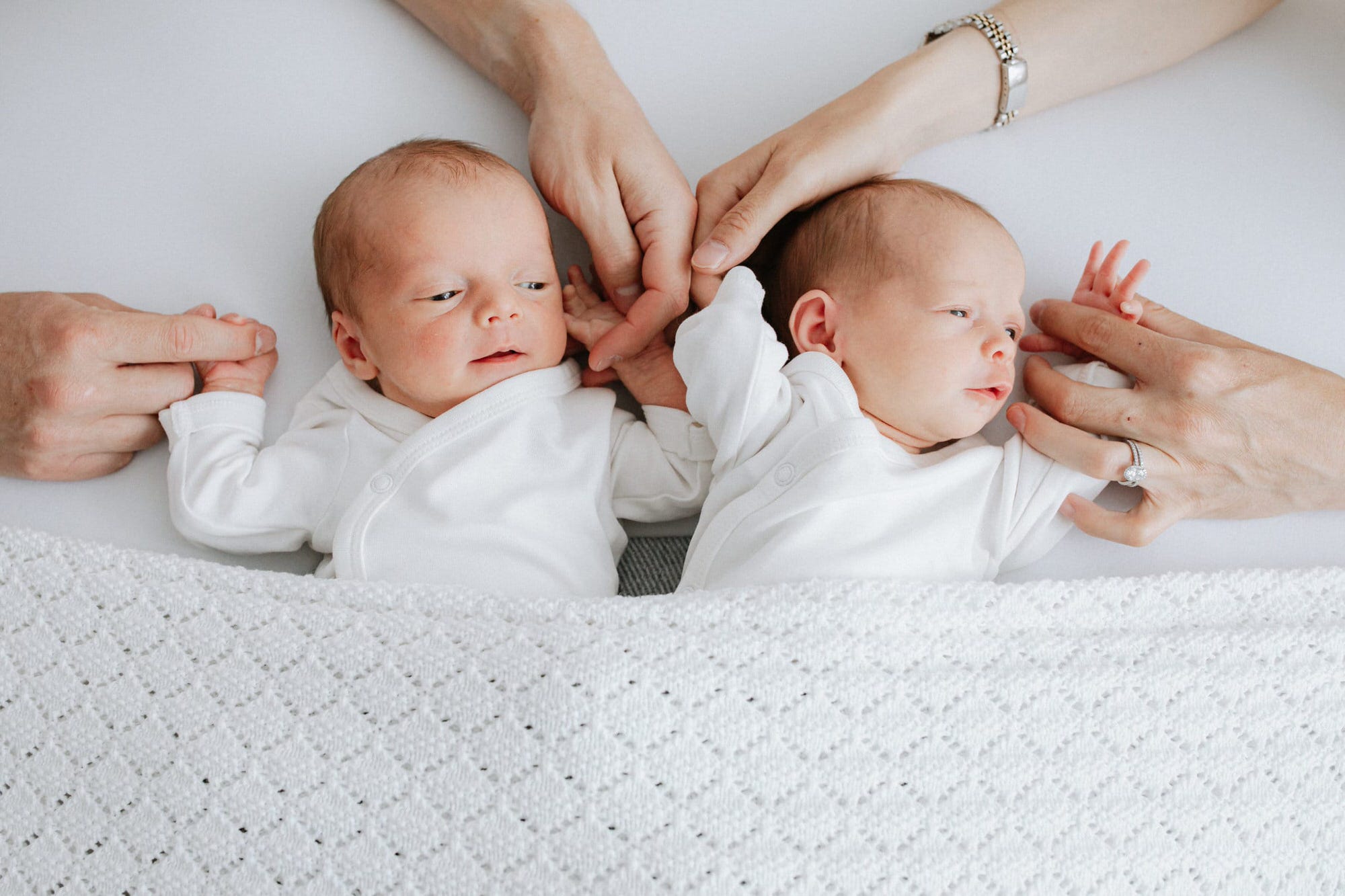 newborn twins in white vests under a white company blanket at their Kent newborn photoshoot in Bexley
