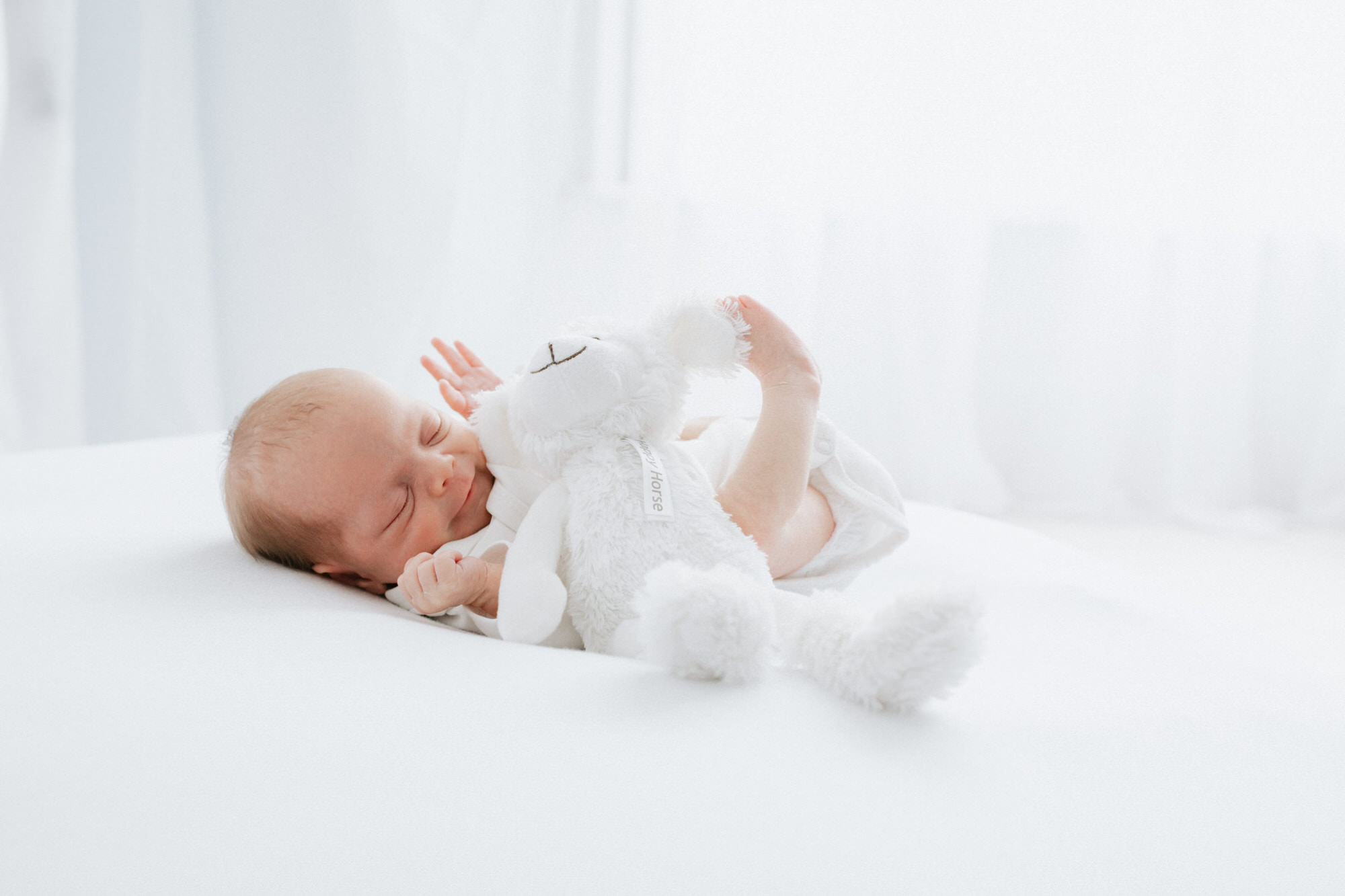 newborn baby cuddling teddy dressed in white at their Kent newborn photoshoot in Bexley