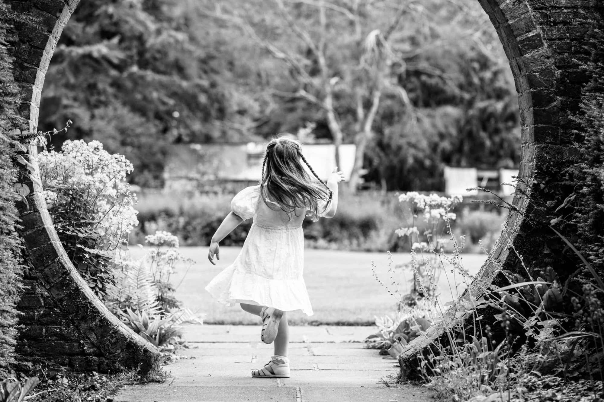 little girl dancing in the iconic archway at Great Comp Gardens at her Kent Family photoshoot in Sevenoaks