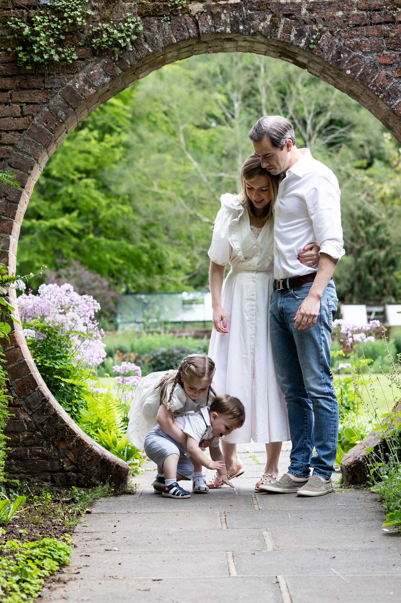 mummy and daddy look down at their children shot in the iconic arch at Great Comp Gardens Sevenoaks on their Kent family photoshoot