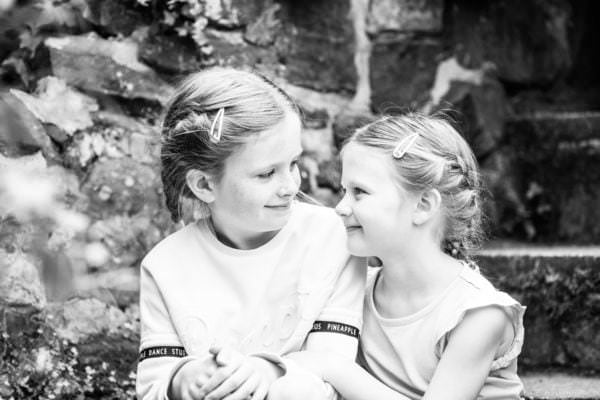 sisters looking at each other sat on a step at their Kent family photoshoot in Sevenoaks