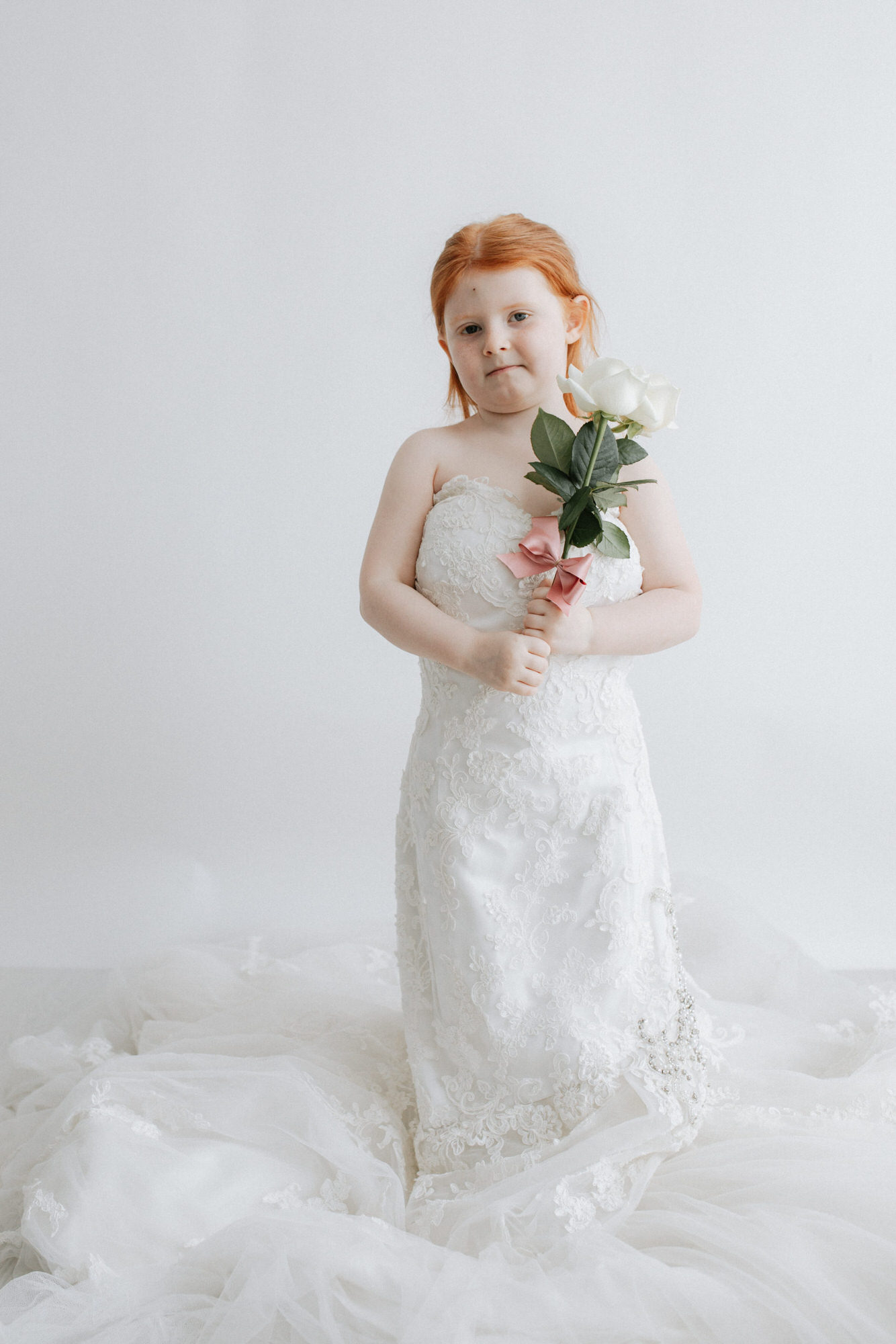 little girl in mummy's wedding dress holding white roses at her Kent photoshoot