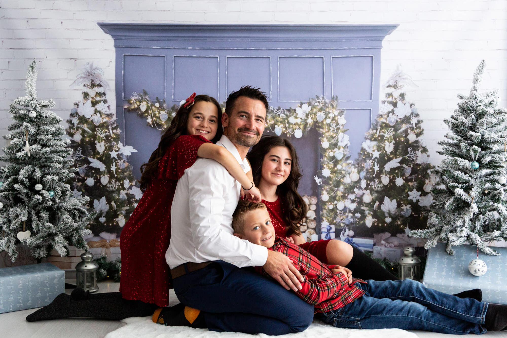 dad with his children sat in front of a blue Christmas fireplace at their Kent Christmas photoshoot in Bexley