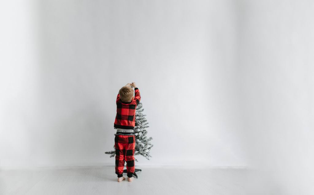 little boy in Christmas pyjamas putting a star on a Christmas tree at his Kent Christmas photoshoot in Bexley
