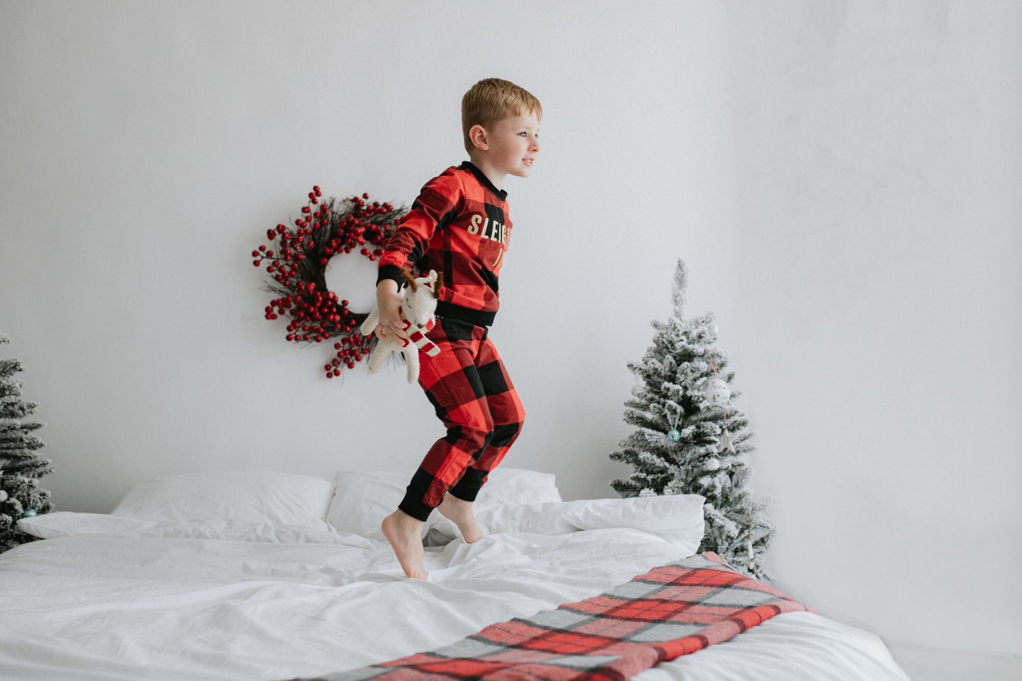 little boy in Christmas pyjamas jumping on the bed at his Christmas photoshoot in Bexley