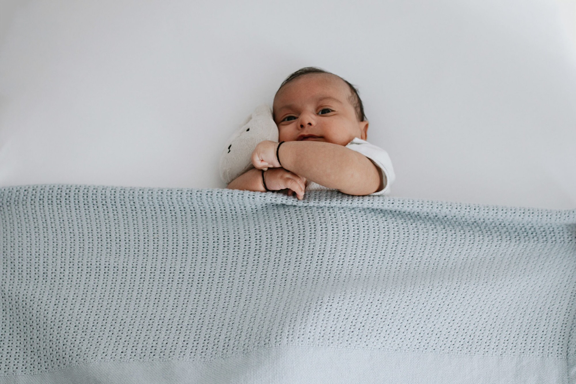 newborn baby boy cuddling teddy under blue blanket at his kent baby photoshoot in bexley