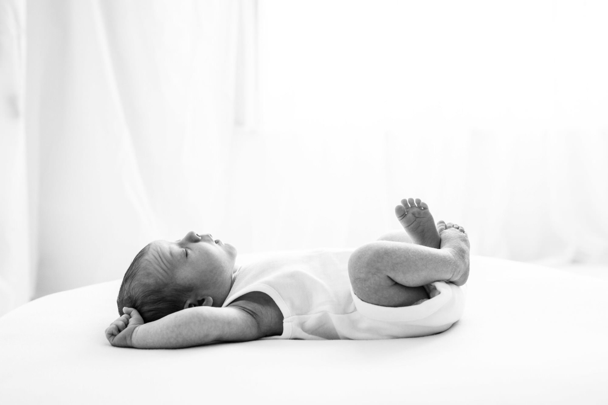 black and white image of newborn baby stretching and frowning at their kent baby photoshoot in bexley