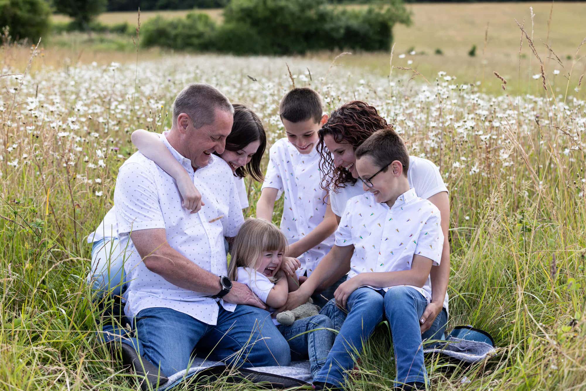 family of 6 tickling the youngest child in a kent wild daisy field at their sevenoaks family photoshoot