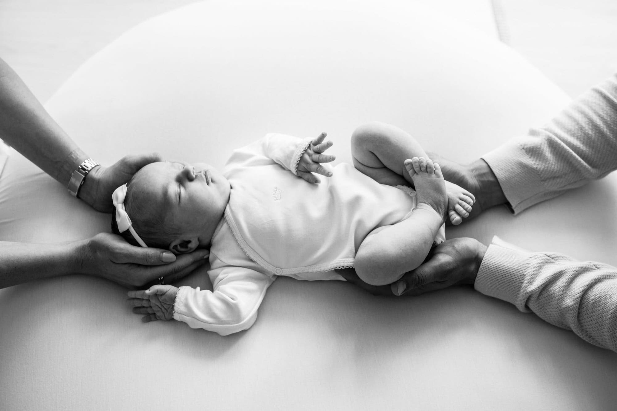 black and white image of a newborn baby in between mummy and daddy's hands at their Kent baby photoshoot in Bexley