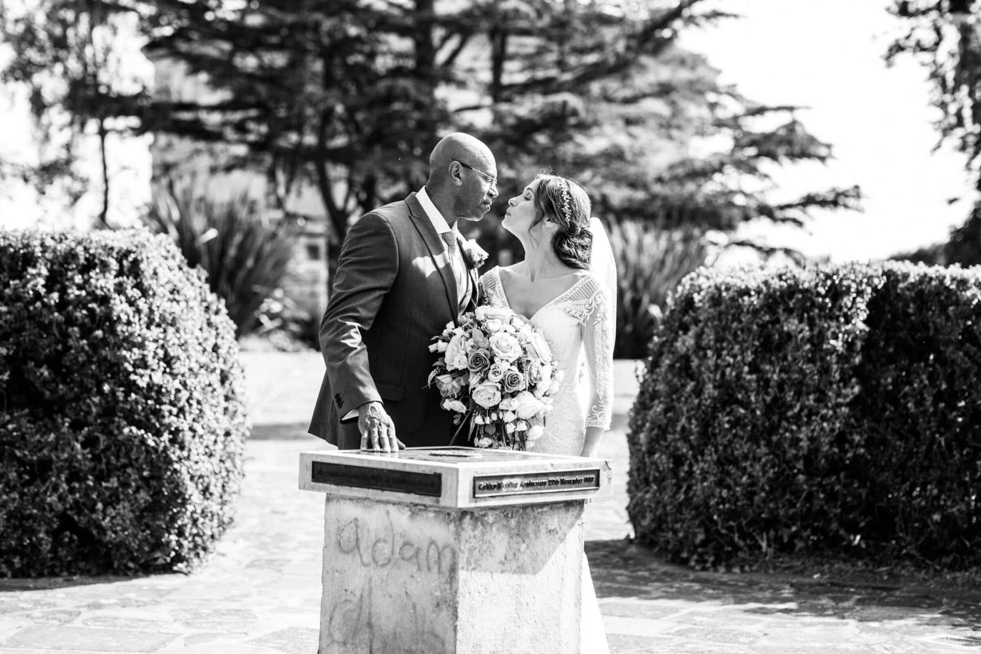 black and white image of bride and groom kissing by sun dial in Danson House Bexleyheath wedding