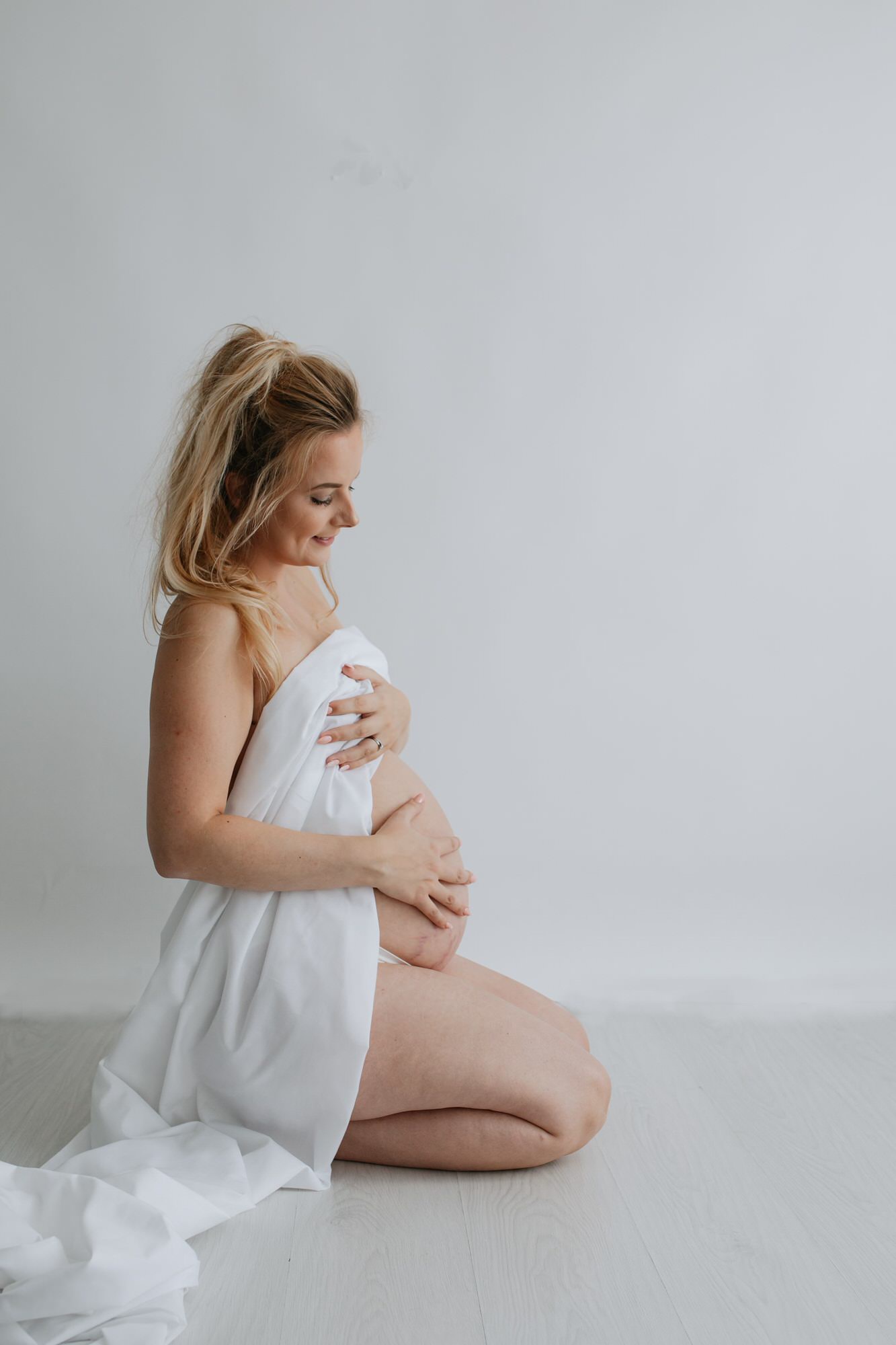 mum to be sat on the floor with white fabric covering her baby bump at her Kent maternity photoshoot in Bexley