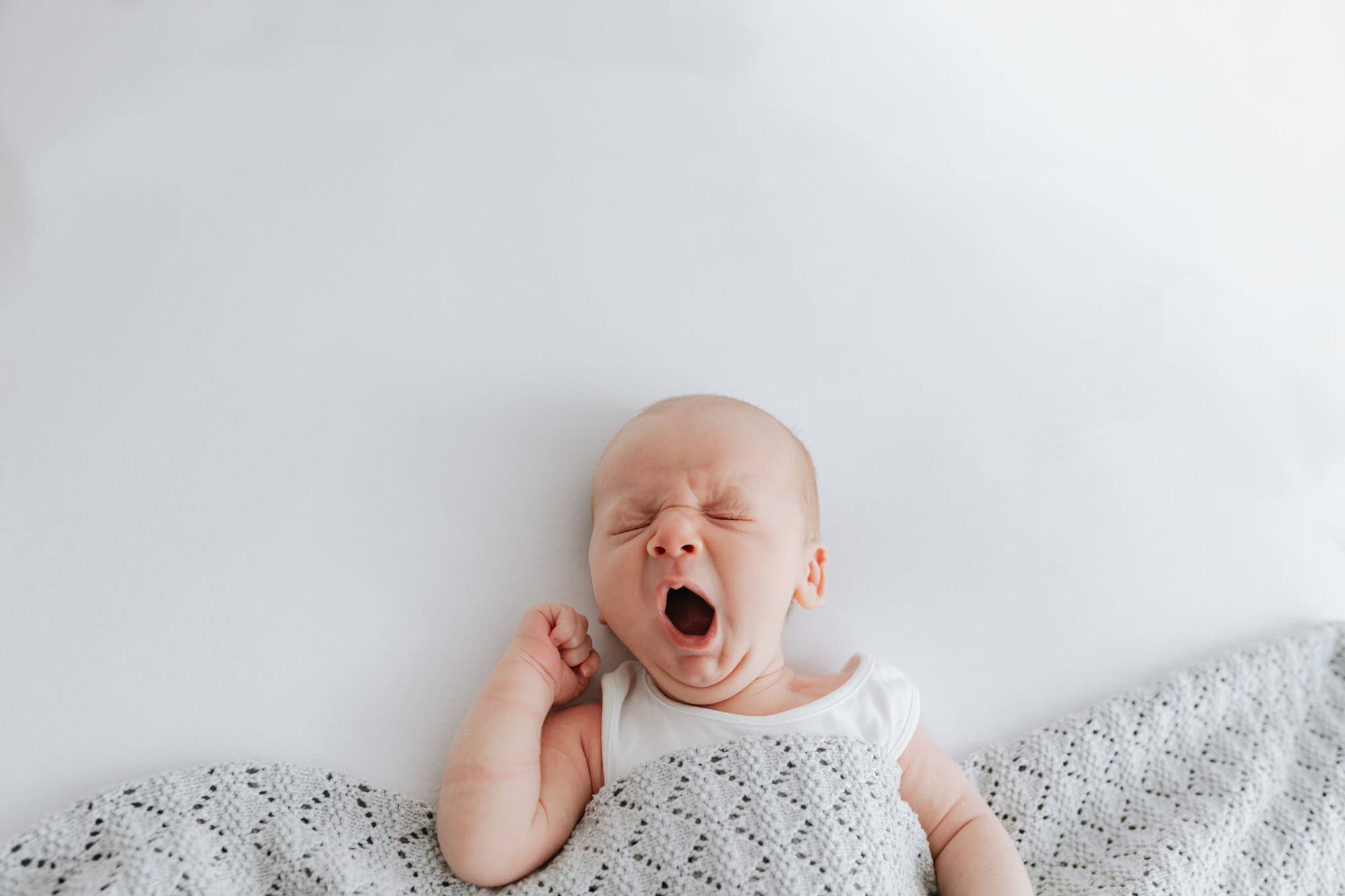 beautiful baby boy yawning wrapped in a white company blanket at his Kent newborn photoshoot in Bexley