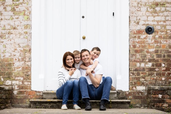 family of four sat on a step infront of rustic white doors and brickwork at their kent spring family photoshoot in Sevenoaks