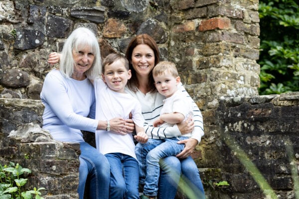 Grandma, mummy and her two boys, sat on a stone wall at their kent extended family photoshoot in Sevenoaks