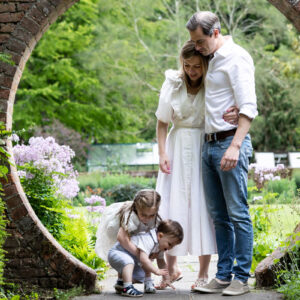 family of 4 with parents watching their two little children playing in an archway at their kent spring photoshoot in Sevenoaks