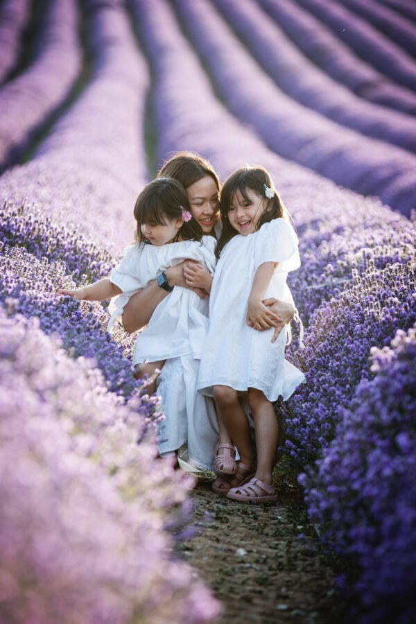 mummy cuddling her two little girls all dressed in white in the beautiful kent lavender fields at their family photoshoot in sevenoaks