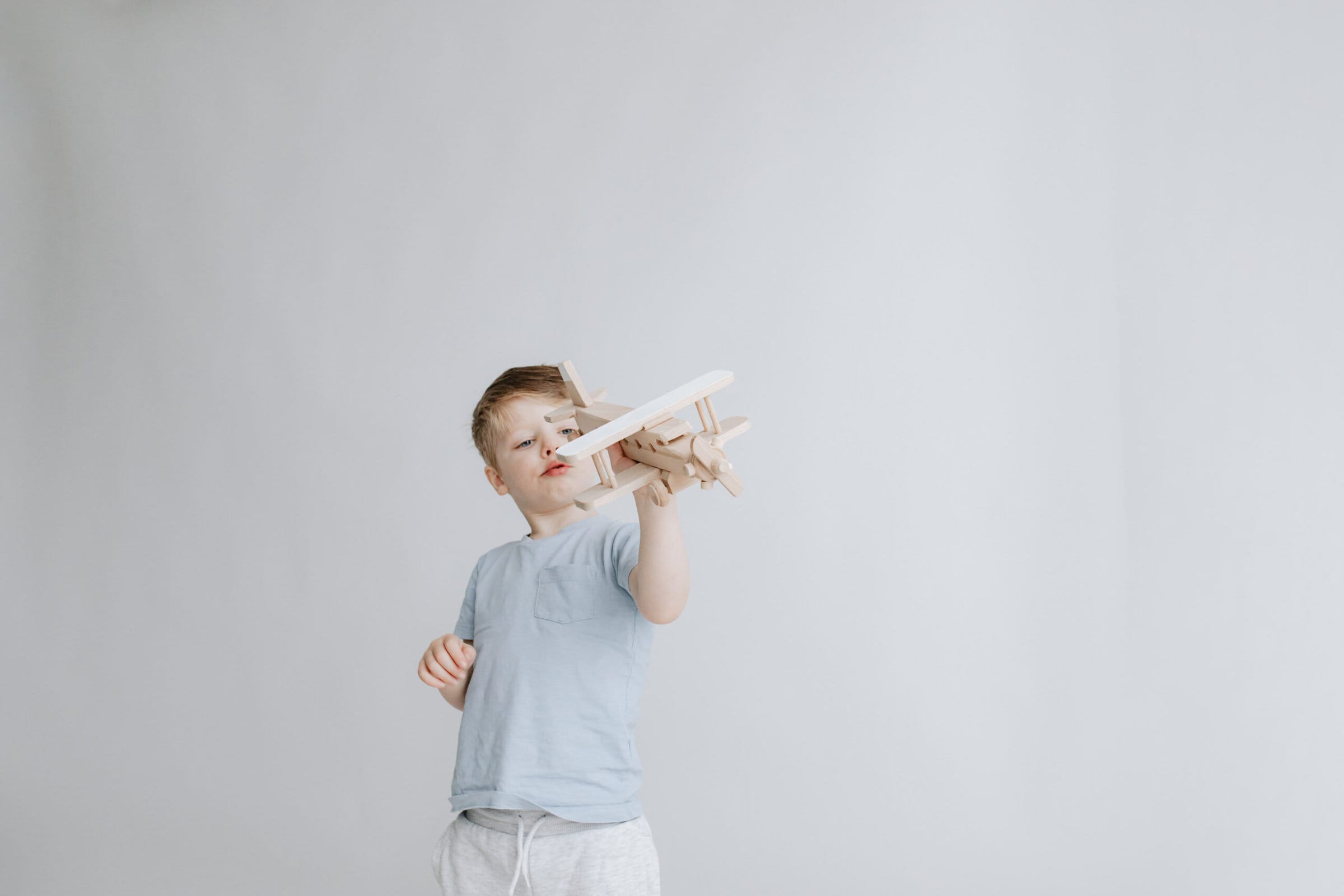 young boy playing with wooden airplane looking at the plane at his kent family photoshoot in bexley