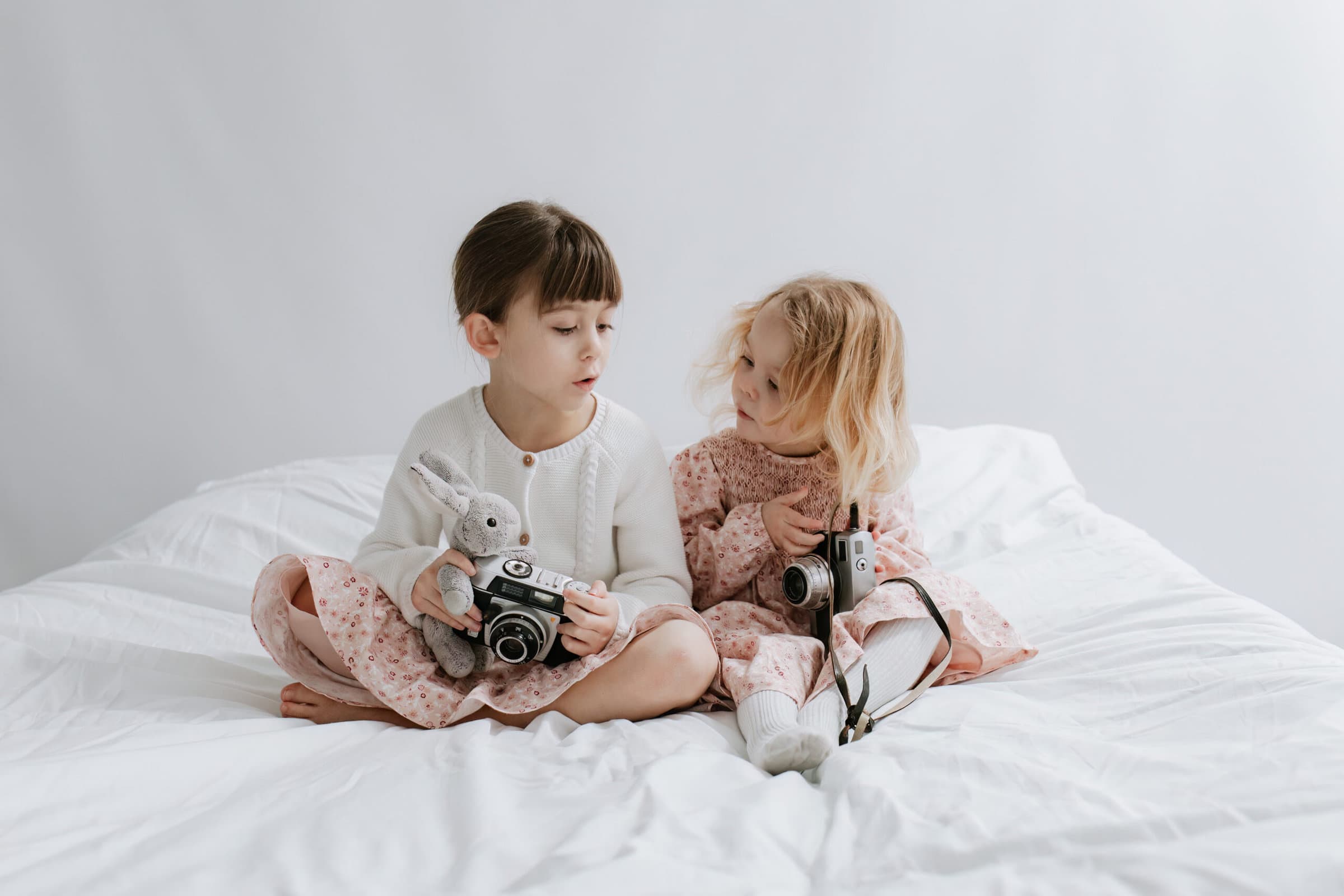 two little girls sat on the bed with vintage cameras at their kent family photoshoot in bexley