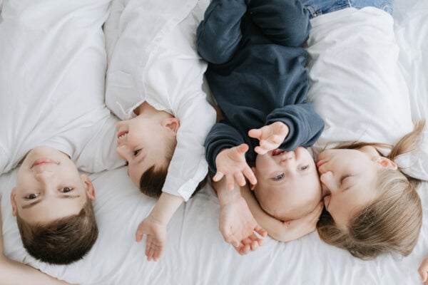 upside down shot of 4 children laid on the bed cuddling at their mummy and me photoshoot in Bexley