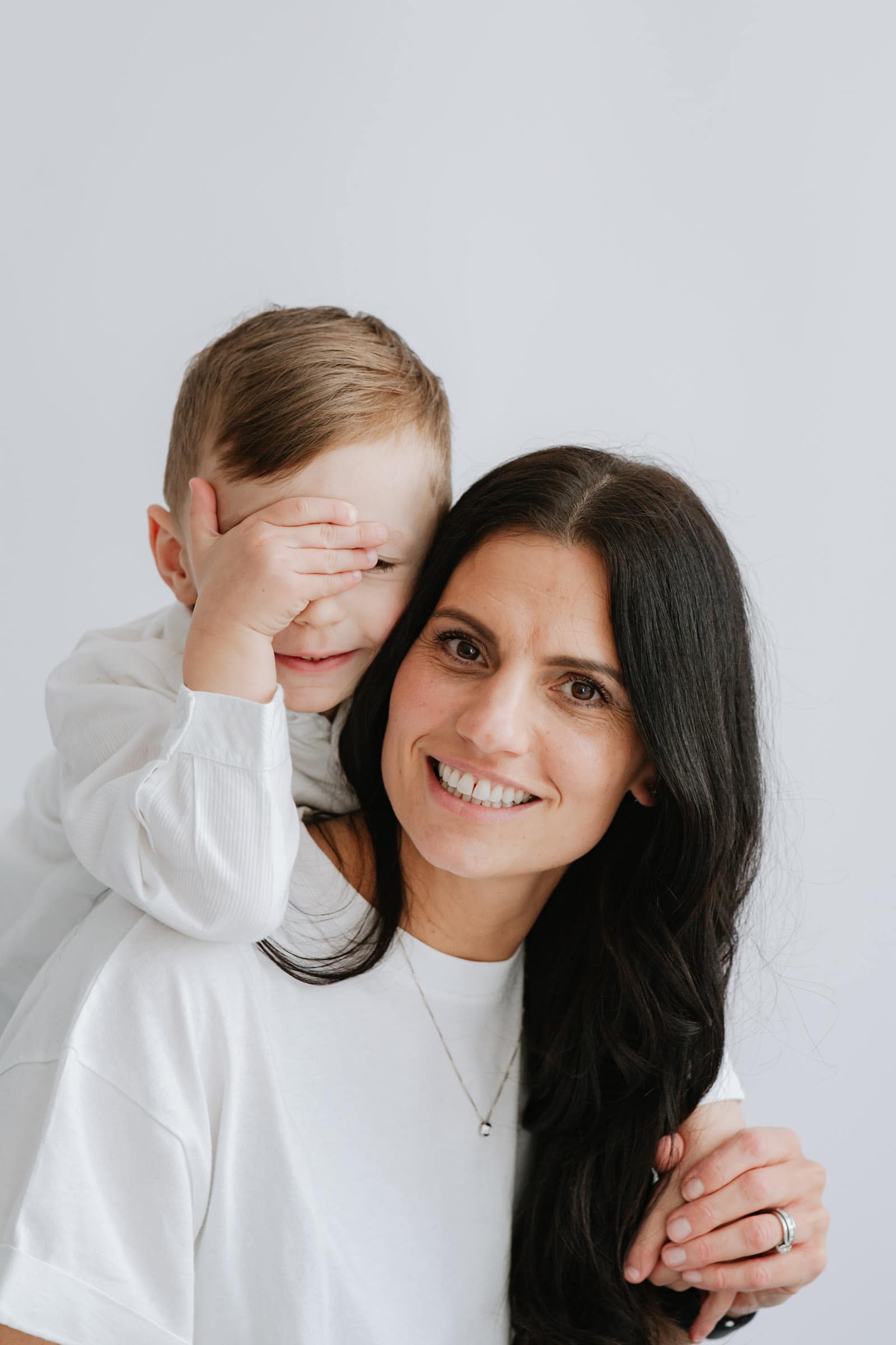 little boy with hand over eyes on mummys shoulders at their bexley family photoshoot in kent