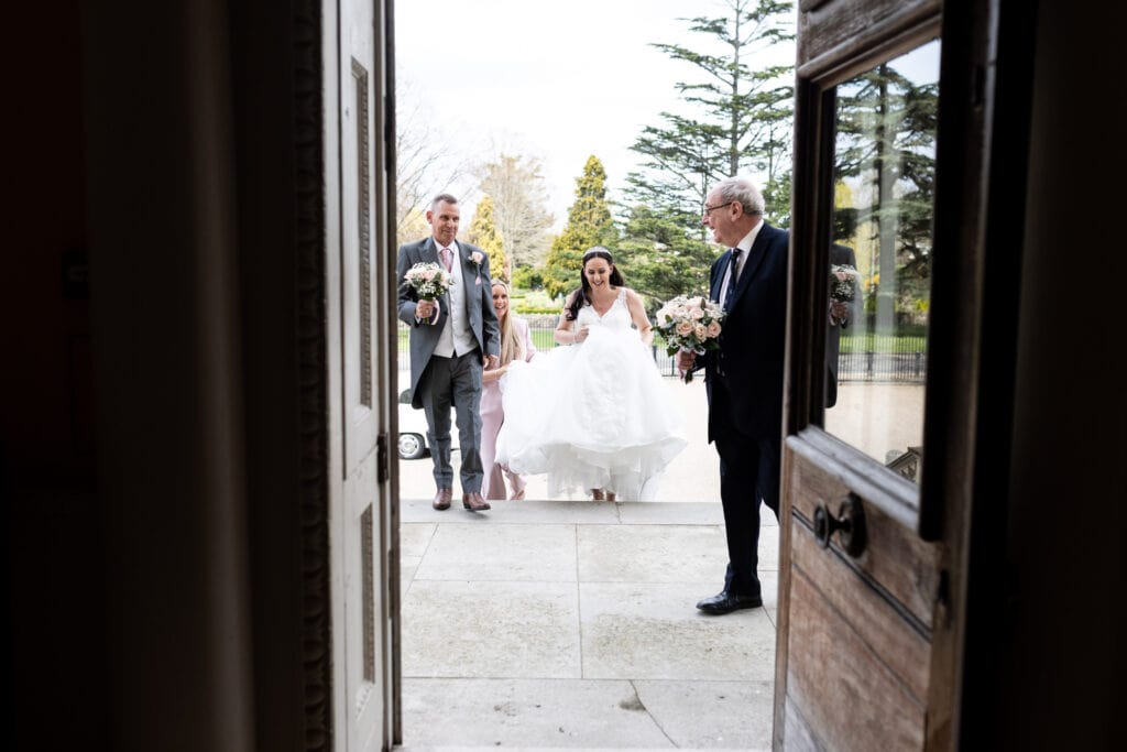 Image shot through the front doorway at Danson House Bexleyheath wedding, bridal party walking up the stairs