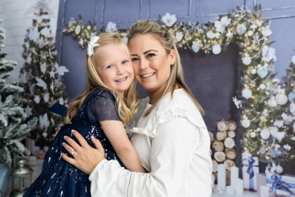 mummy and daughter having a cuddle infront of a christmas fireplace at their bexley christmas mini photoshoot